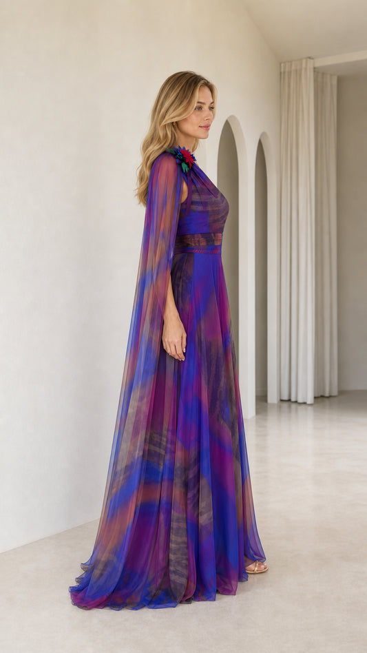 Side profile view of royal blue chiffon cape gown showing dramatic floor-sweeping cape sleeve