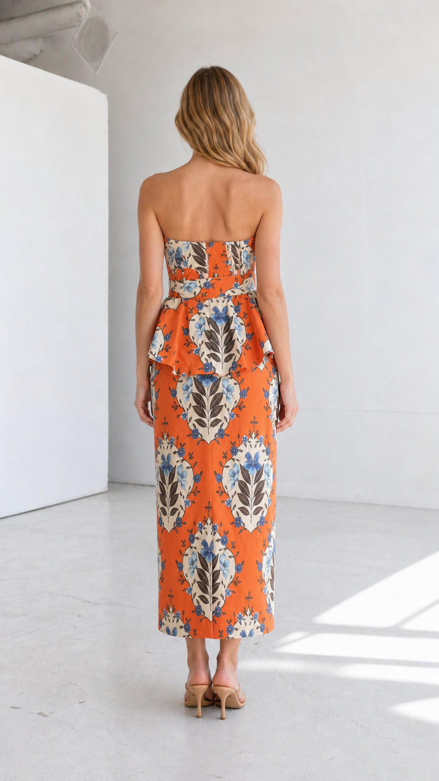 Back view of model in orange strapless floral midi dress