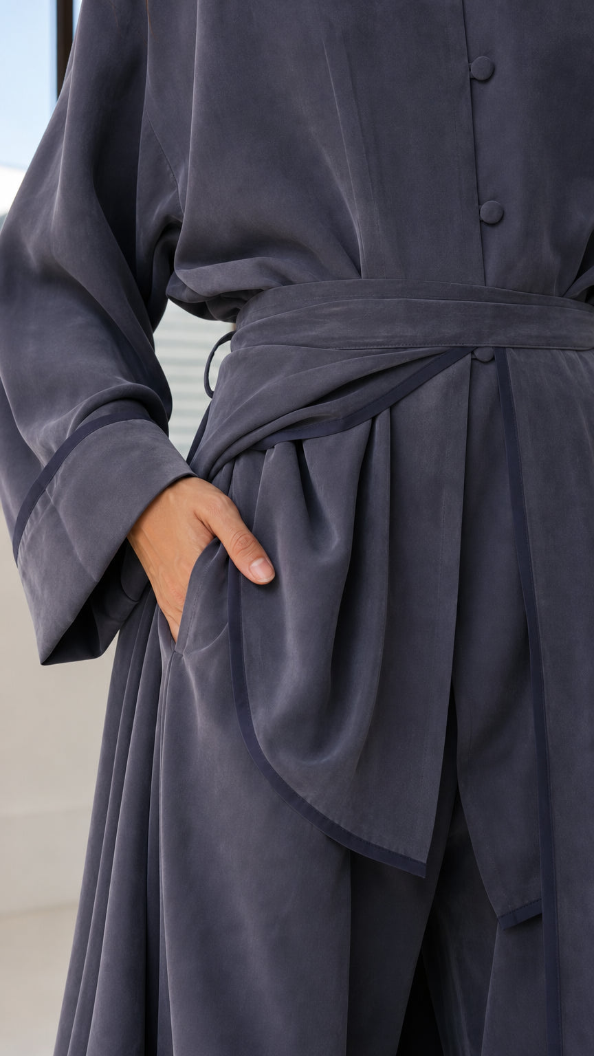 Close-up detail of smooth slate blue fabric, front buttons, side pocket, and draped sash tie