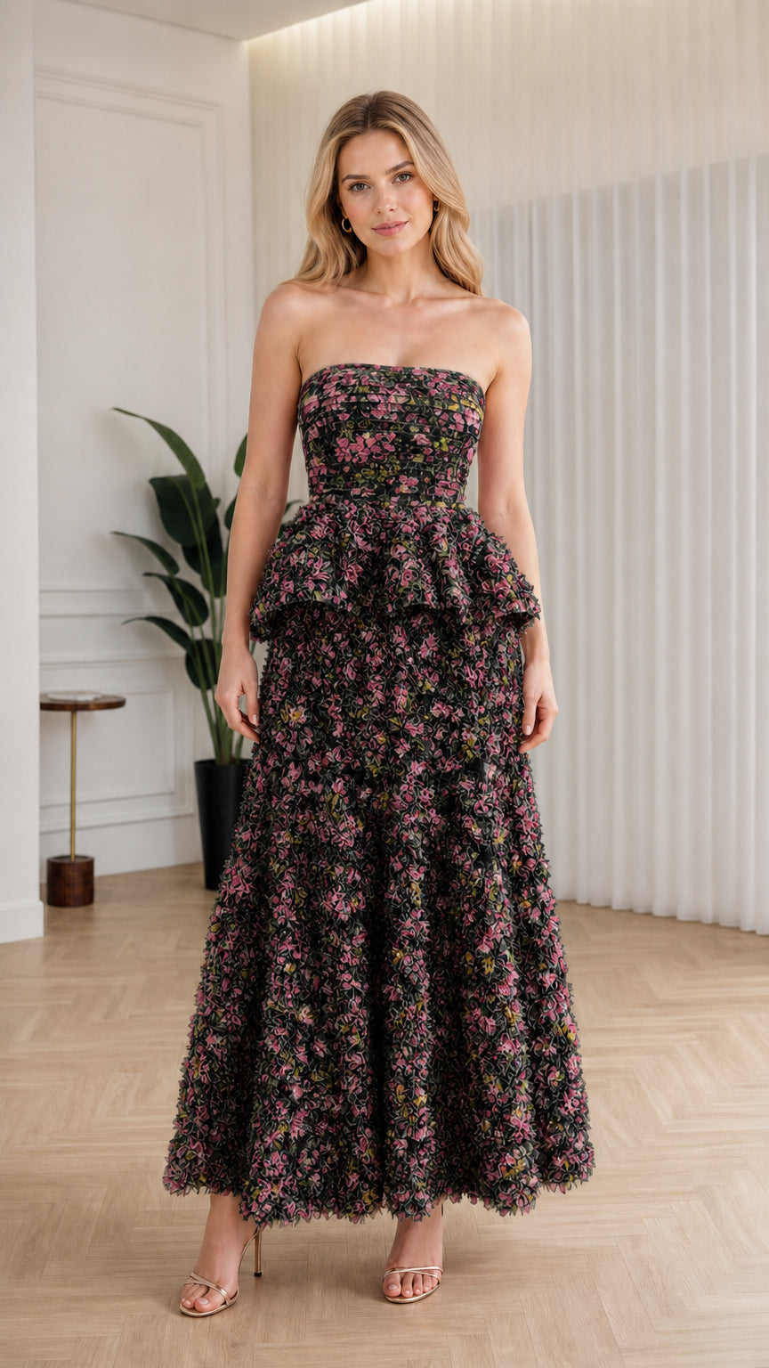 Front view of model wearing black floral strapless ruffle peplum maxi dress